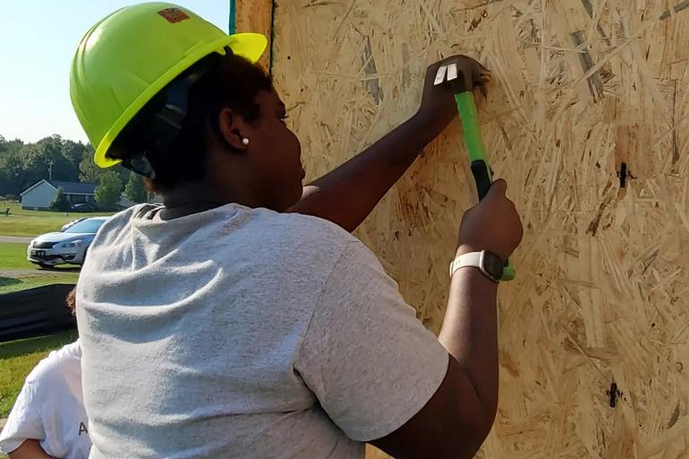 Student working to build a house with hammer in right hand.