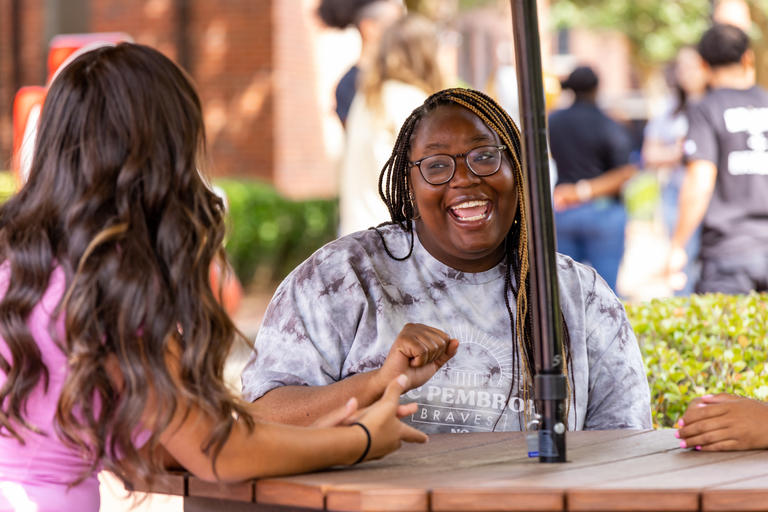 Two female students laughing and talking in the quad